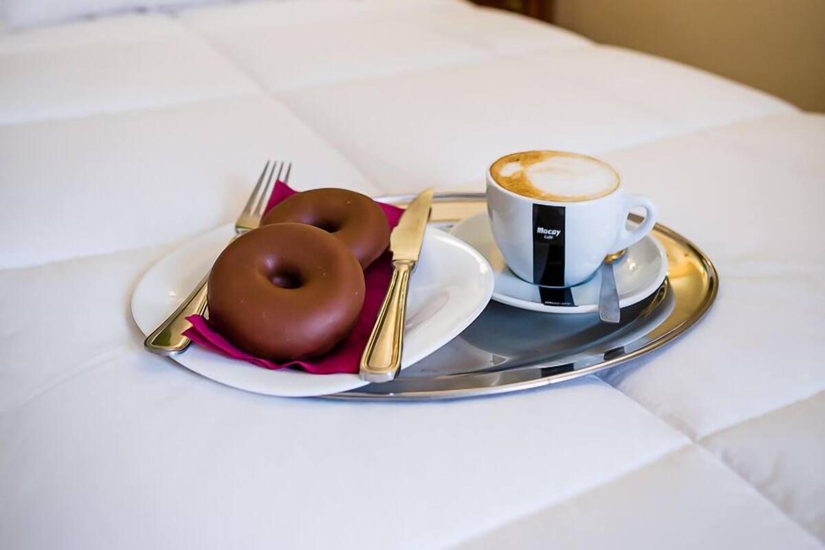 Una cama bien hecha con una bandeja que contiene un donut, una taza de café y cubiertos.