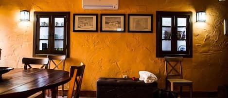 A dining area with wooden tables and chairs, a black cushioned bench, and a wall-mounted air conditioner.
