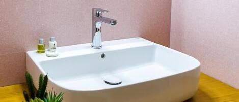 A bathroom with a white sink, a wooden countertop, a mirror with a wooden frame, and a small potted plant on the counter.