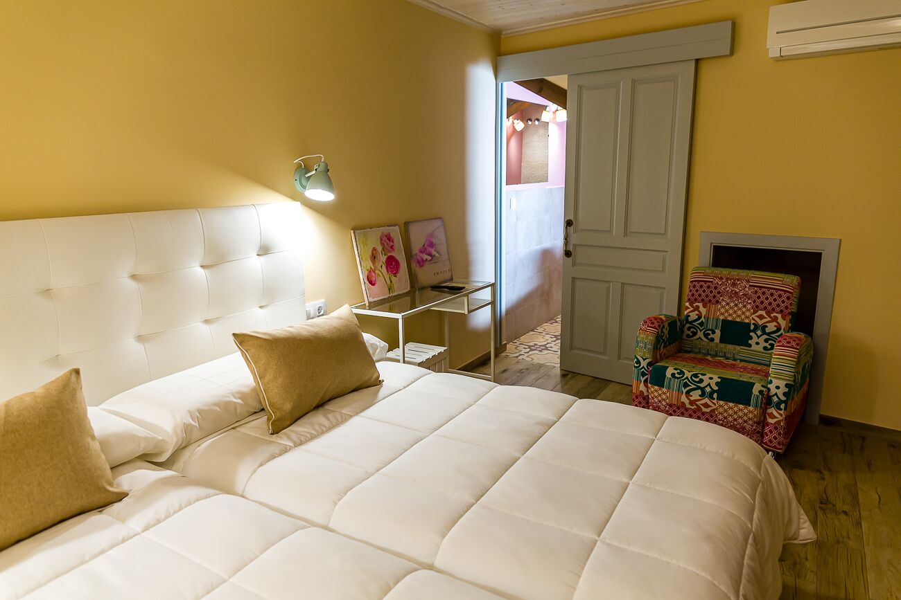 A bedroom with a large bed, a bedside table, a chair, and a door.