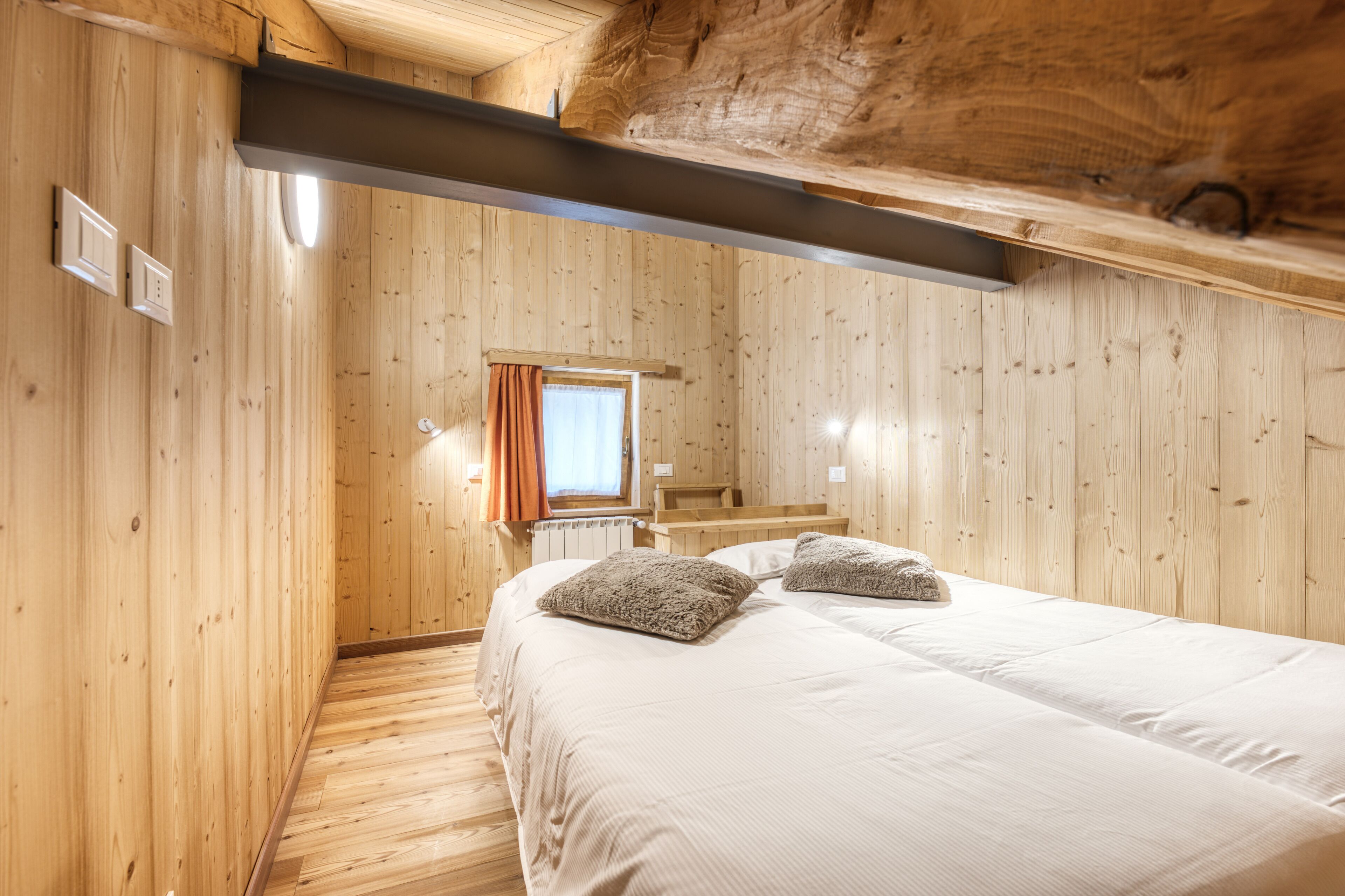 Ein Zimmer mit Holzwänden, einem Bett, einem Fenster mit Vorhängen und einer hölzernen Bank.
