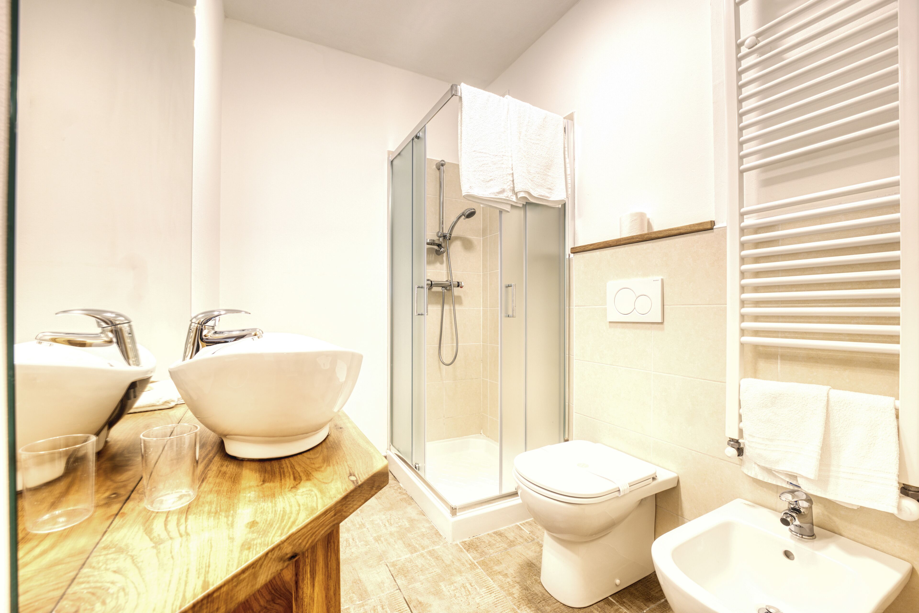 Un baño con tocador de madera, dos lavamanos, cabina de ducha de vidrio, inodoro y bidé.