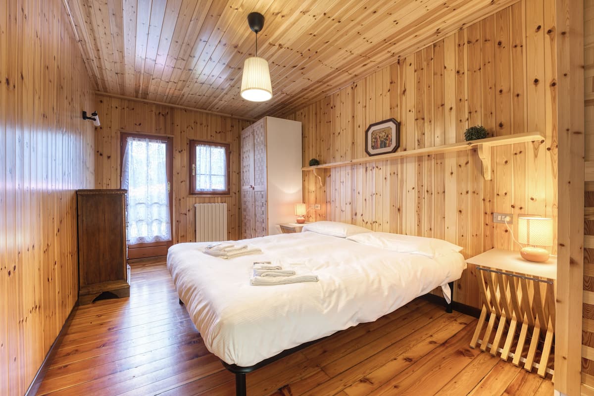 A wooden-paneled bedroom with a large bed, bedside tables, a wardrobe, and a window.