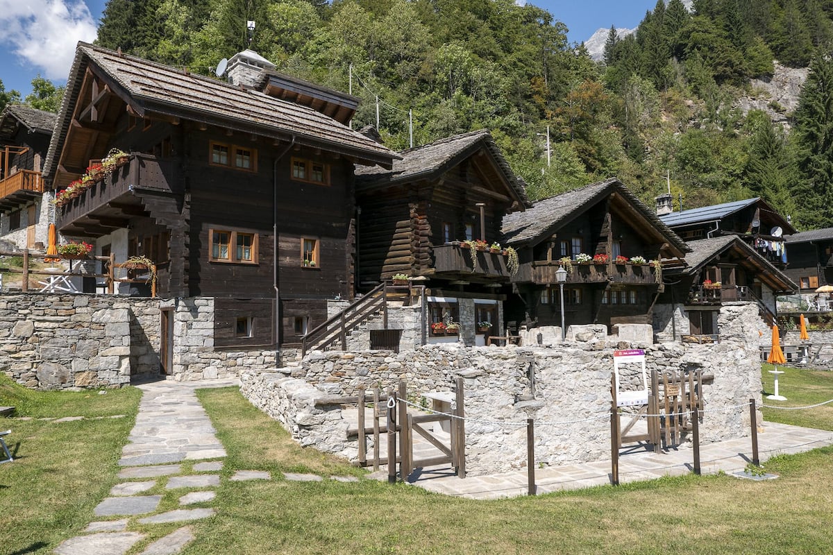 A traditional wooden chalet with stone walls, a stone pathway, and a wooden gate.
