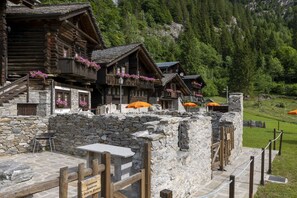 Una cabaña de madera tradicional con paredes de piedra, balcones con macetas de flores y una mesa de piedra en primer plano.