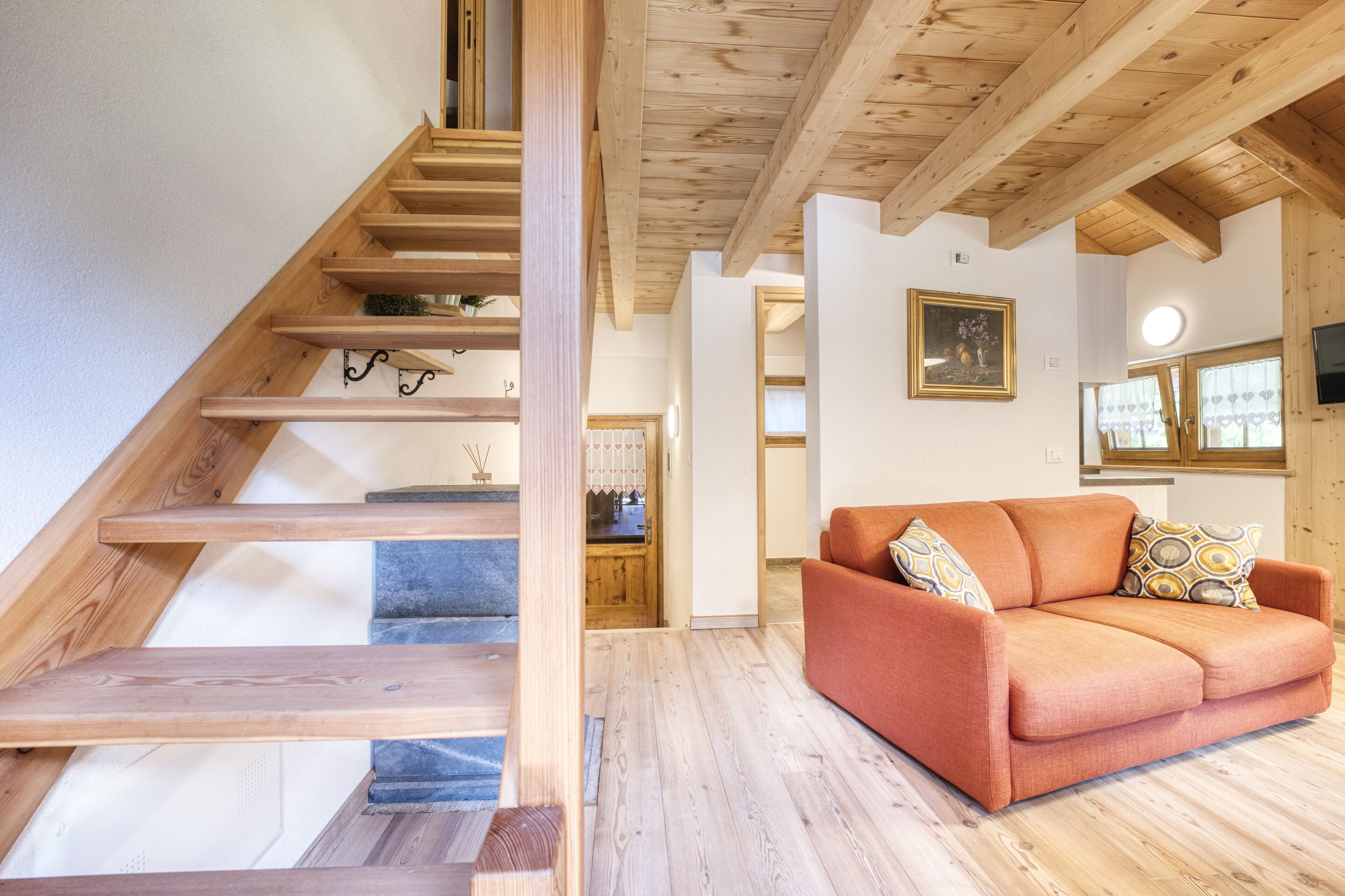 Eine Holztreppe führt zu einem Wohnbereich mit einer Couch und einem Bild an der Wand.