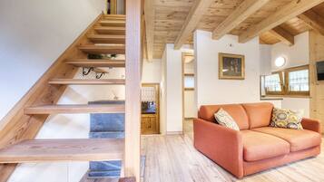 Eine Holztreppe führt zu einem Wohnbereich mit einer Couch und einem Bild an der Wand.