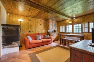 Una habitación acogedora con techo de madera, chimenea, sofá, mesa de madera y ventana con vistas.