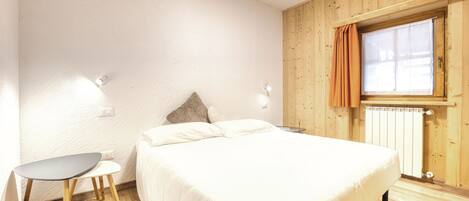 A bedroom with a bed, a small table, and a window with curtains.