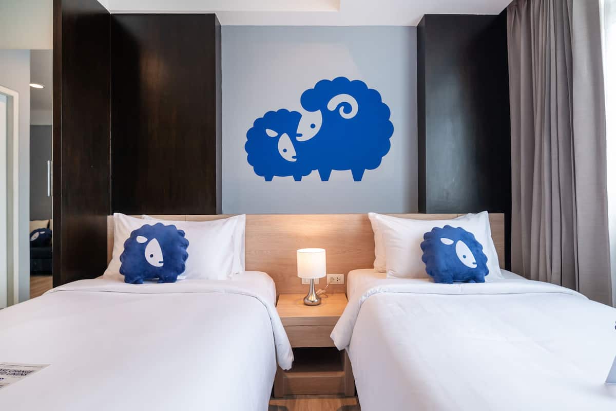 A hotel room with two beds, a nightstand with a lamp, and a wall decoration of sheep.
