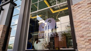 A modern building with a glass facade, a visible logo, and a brick wall. - Kokotel Bangkok Dheva Thonglor (Bangkok)