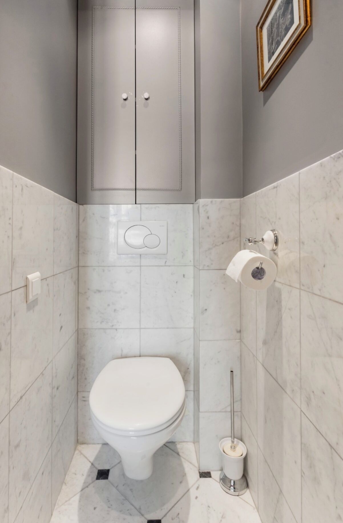 A small, modern bathroom with a toilet, a toilet paper holder, and a mop.