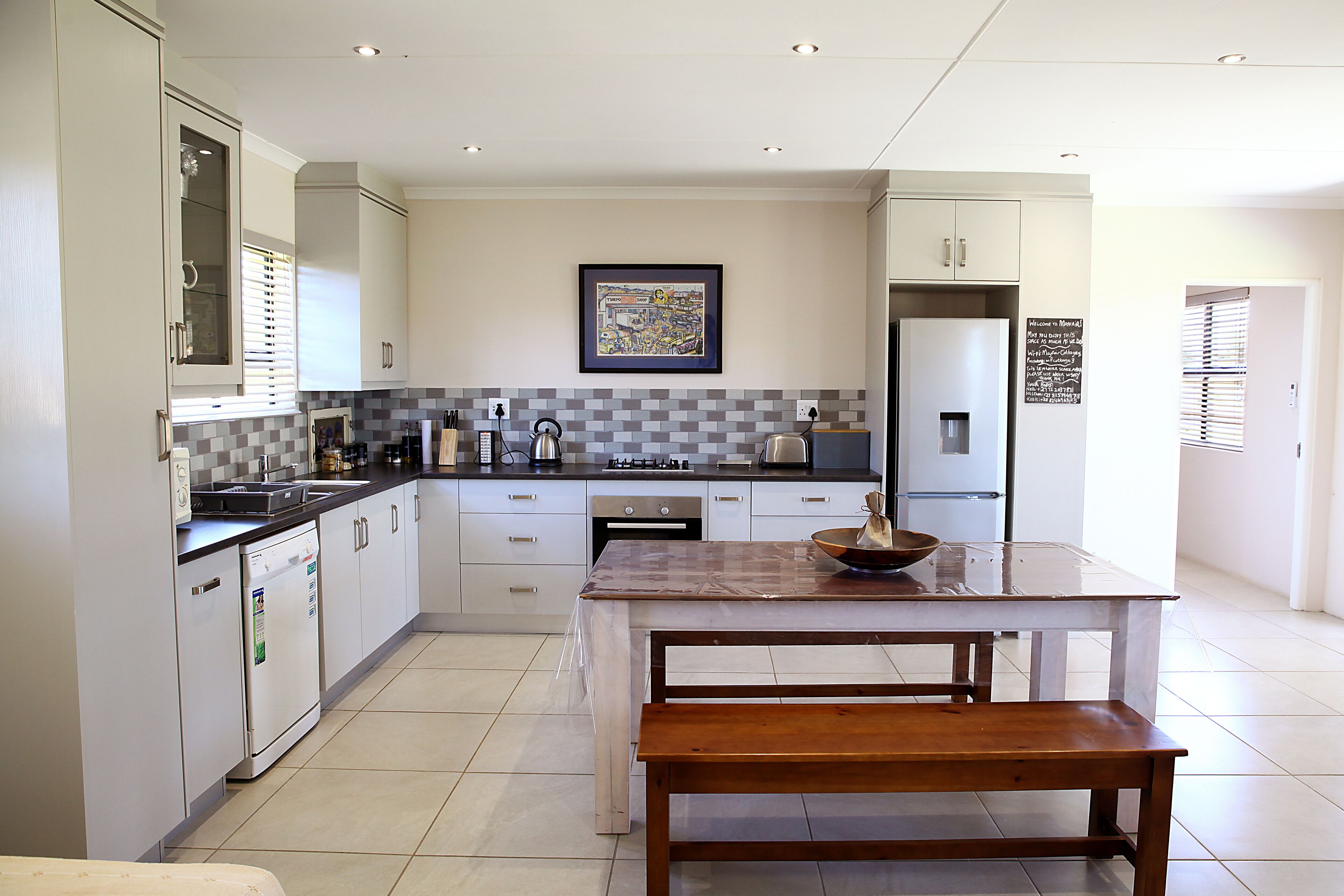 A modern kitchen with white cabinets, a tiled backsplash, and a wooden dining table with a bench.
