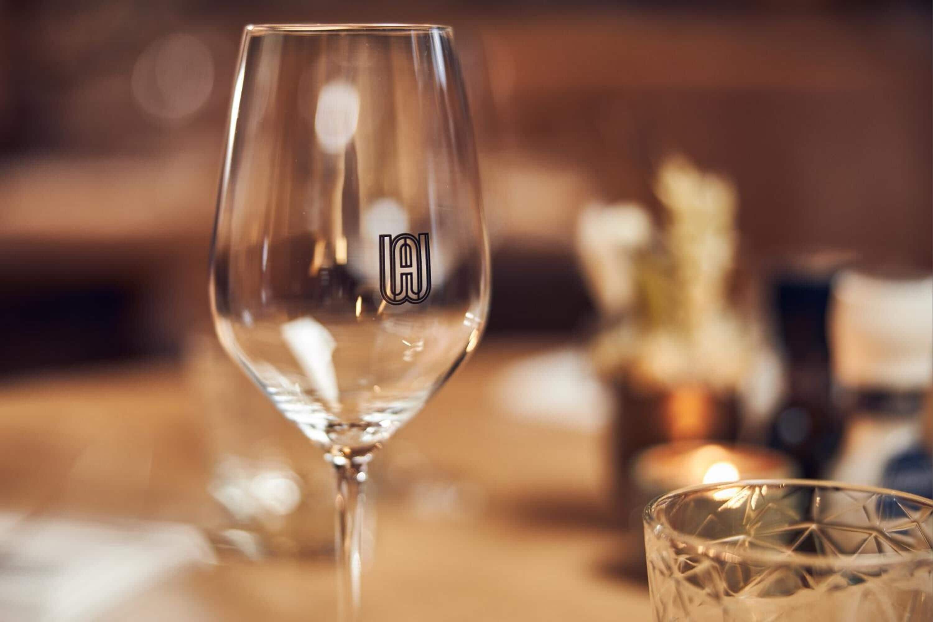 Una copa de vidrio transparente con un logotipo, sobre una mesa con fondo desenfocado.