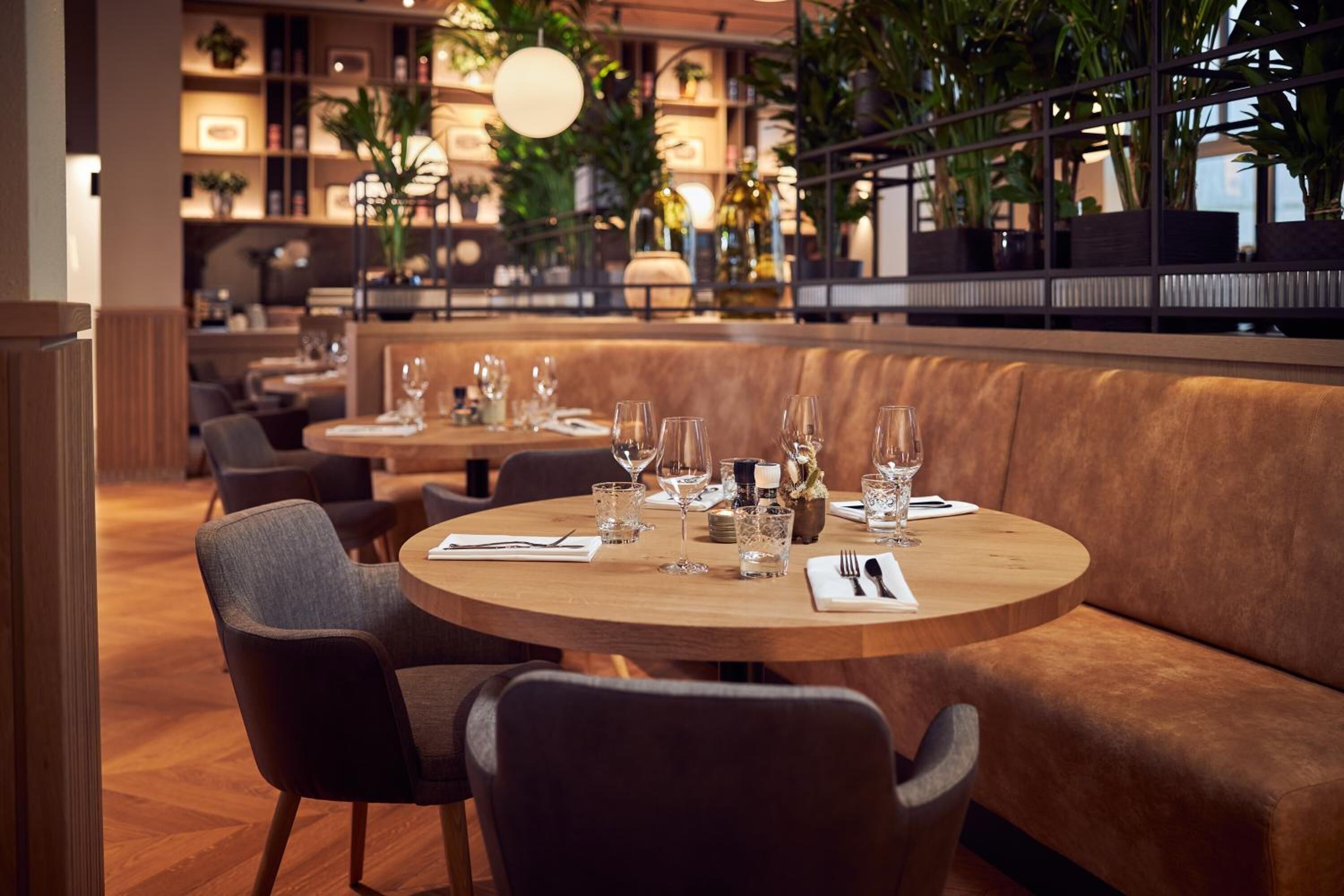 Een restaurant met ronde tafels, comfortabele zittingen en binnenshuis planten.