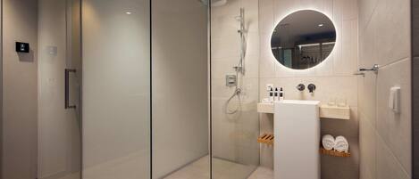 A modern bathroom with a glass-enclosed shower, a round mirror, a sink, and a shelf with towels.