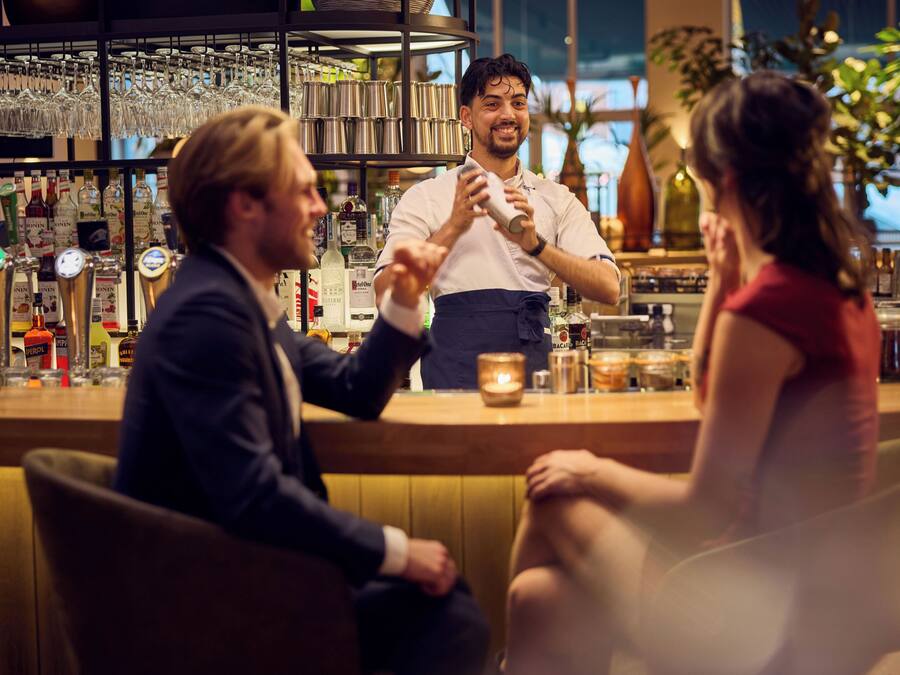 Un bar con un cantinero, un hombre sentado y una mujer.