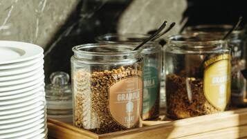 A breakfast buffet setup with various food items in glass jars, plates stacked on the side, and a wooden serving tray.