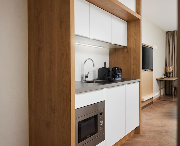 Una cocina moderna con armarios blancos, un lavamanos de acero inoxidable, una cafetera y un horno empotrado.
