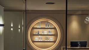 Uma área de recepção com uma vitrine circular de certificados ou prêmios embutidos em prateleiras, um balcão de atendimento e um painel de vidro.