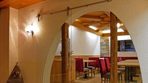 A dining area with a wooden ceiling, red upholstered chairs, and a stone wall in the background. - Hotel Grieserhof (Lermoos)