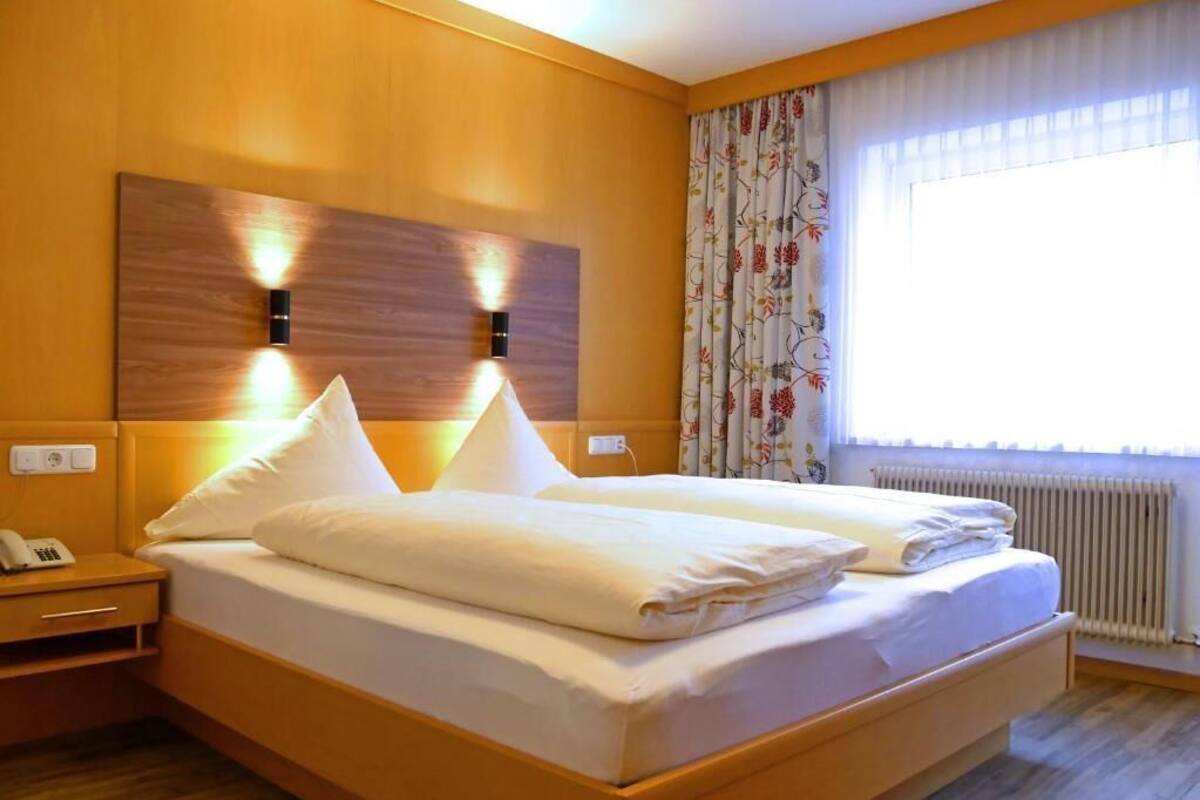 A double bed with two pillows, a bedside table with a phone, and a window with curtains.