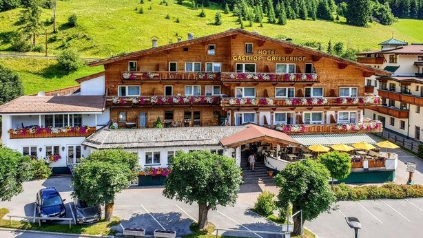 A hotel with a wooden facade, multiple balconies with flower boxes, and a parking area in front. - Hotel Grieserhof (Lermoos)