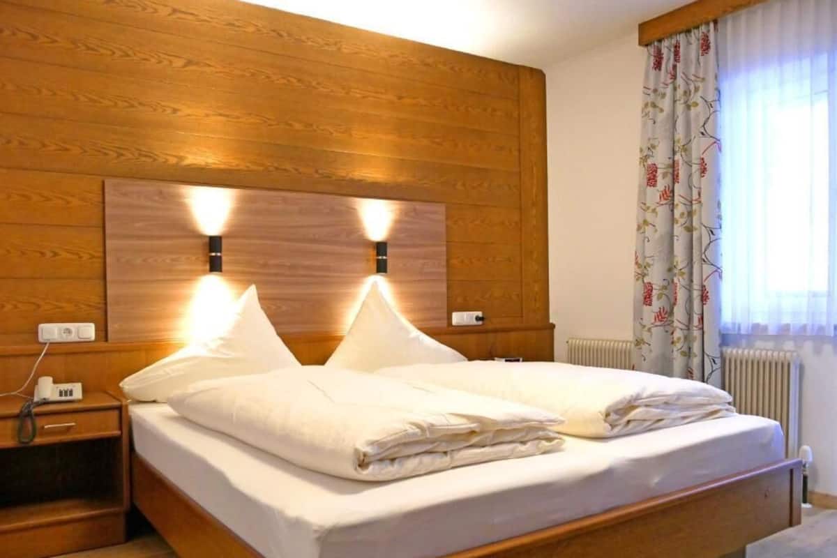 A double bed with a wooden headboard, two bedside tables, and a window with floral curtains.