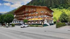 A hotel with a traditional Alpine architectural style, featuring multiple balconies with flower boxes, a covered outdoor seating area, and a view of a mountainous landscape. - Hotel Grieserhof (Lermoos)