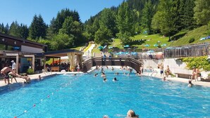 A swimming pool with people swimming and sunbathing, surrounded by a mountainous landscape. - Hotel Grieserhof (Lermoos)