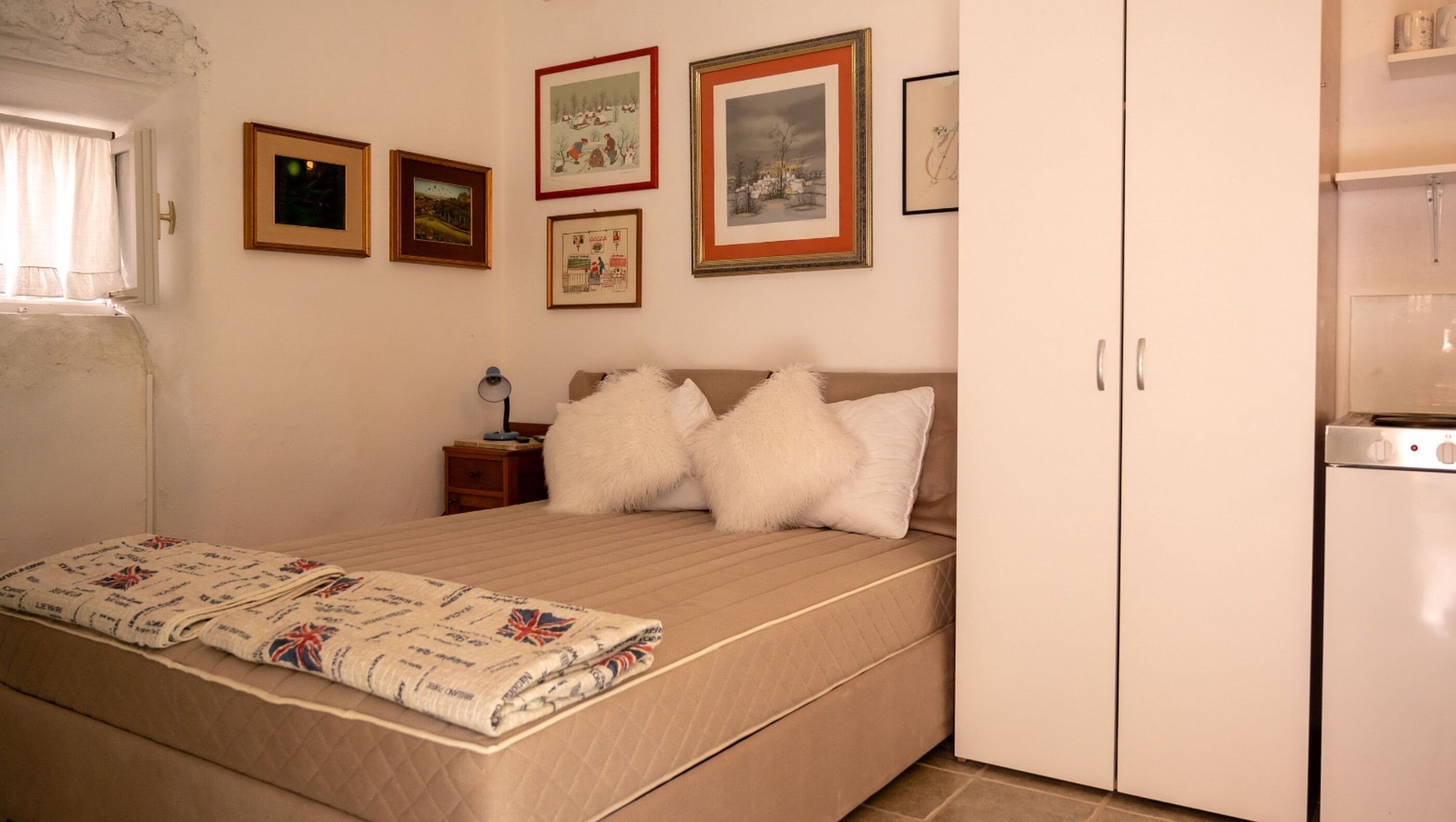 A bedroom with a bed, pillows, a nightstand, a lamp, and framed pictures on the wall.
