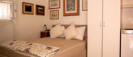 A bedroom with a bed, pillows, a nightstand, a lamp, and framed pictures on the wall.