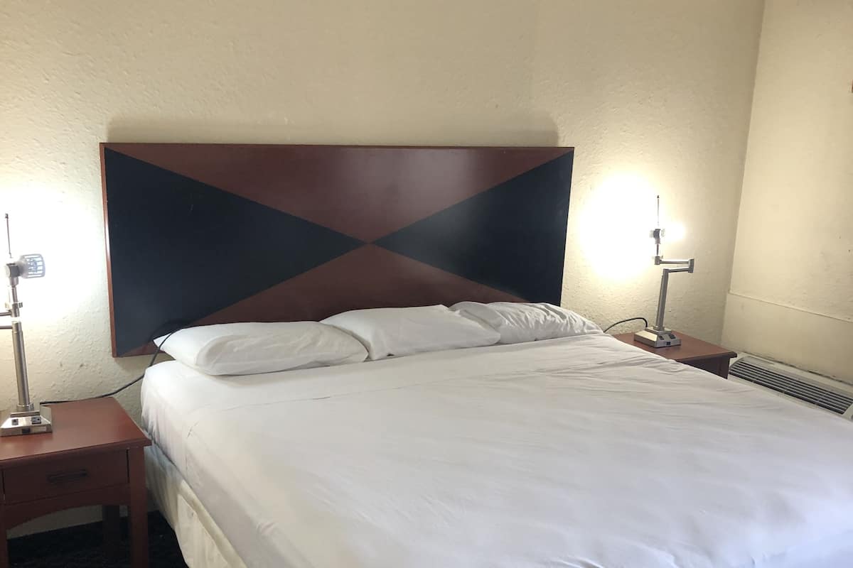 Una habitación de hotel con una cama grande, dos mesitas de noche, una lámpara de pared y un radiador.