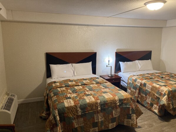 A hotel room with two beds, each with a wooden headboard and white bedding. There is a nightstand with a lamp between the beds. - Petersburg VA Hotel (Petersburg)
