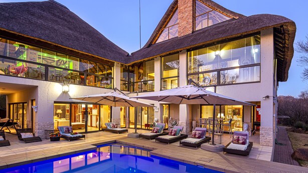 A modern two-story house with a large glass facade, a swimming pool, and outdoor seating areas. - Vaal River YOLO Spaces – Vaal River Bush Lodge (Metsimaholo)