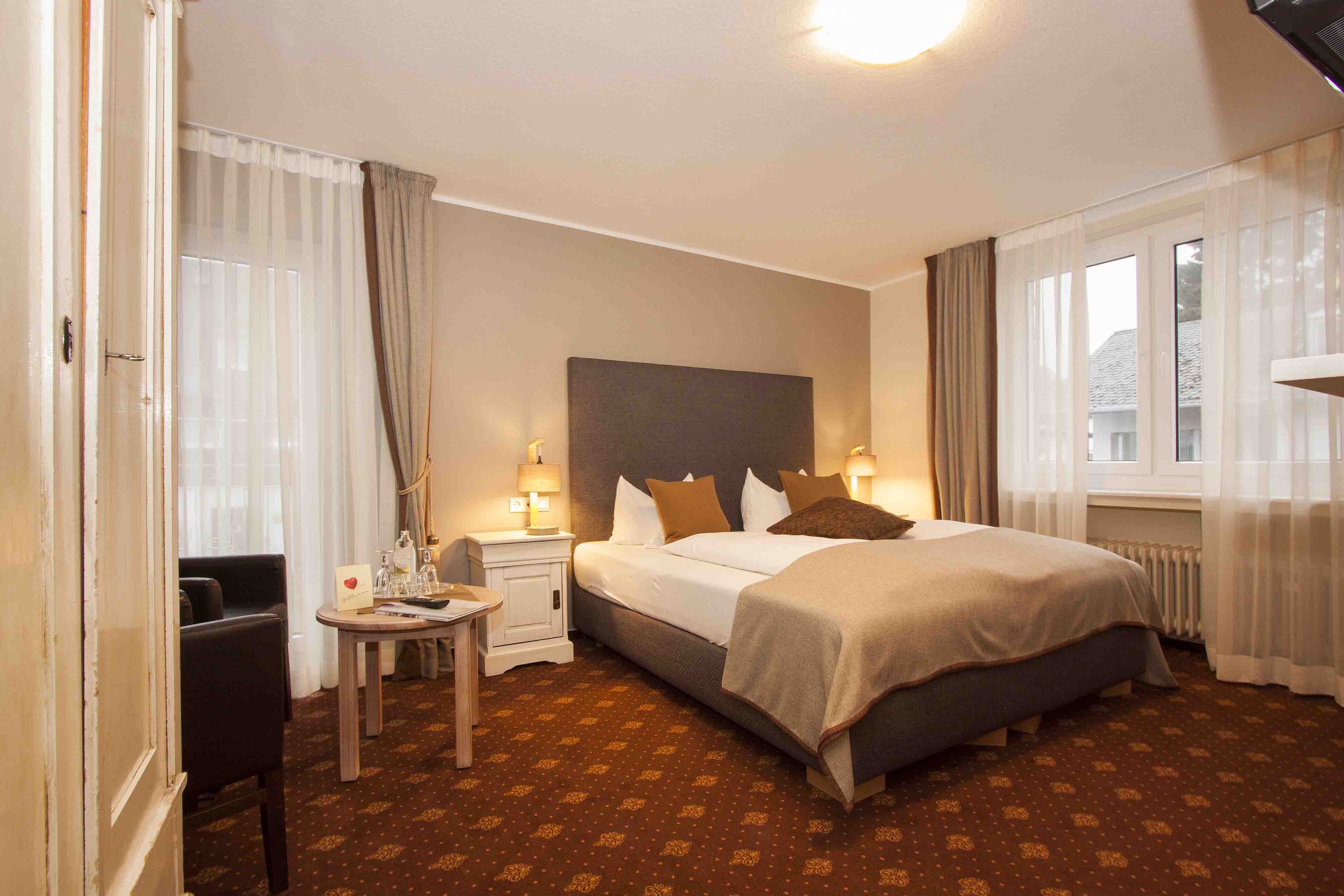 Una habitación de hotel con una cama grande, una mesita de noche, una silla y una ventana con cortinas.