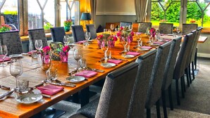 Una larga mesa de comedor lista para una comida, con sillas, vasos y centros de mesa florales.