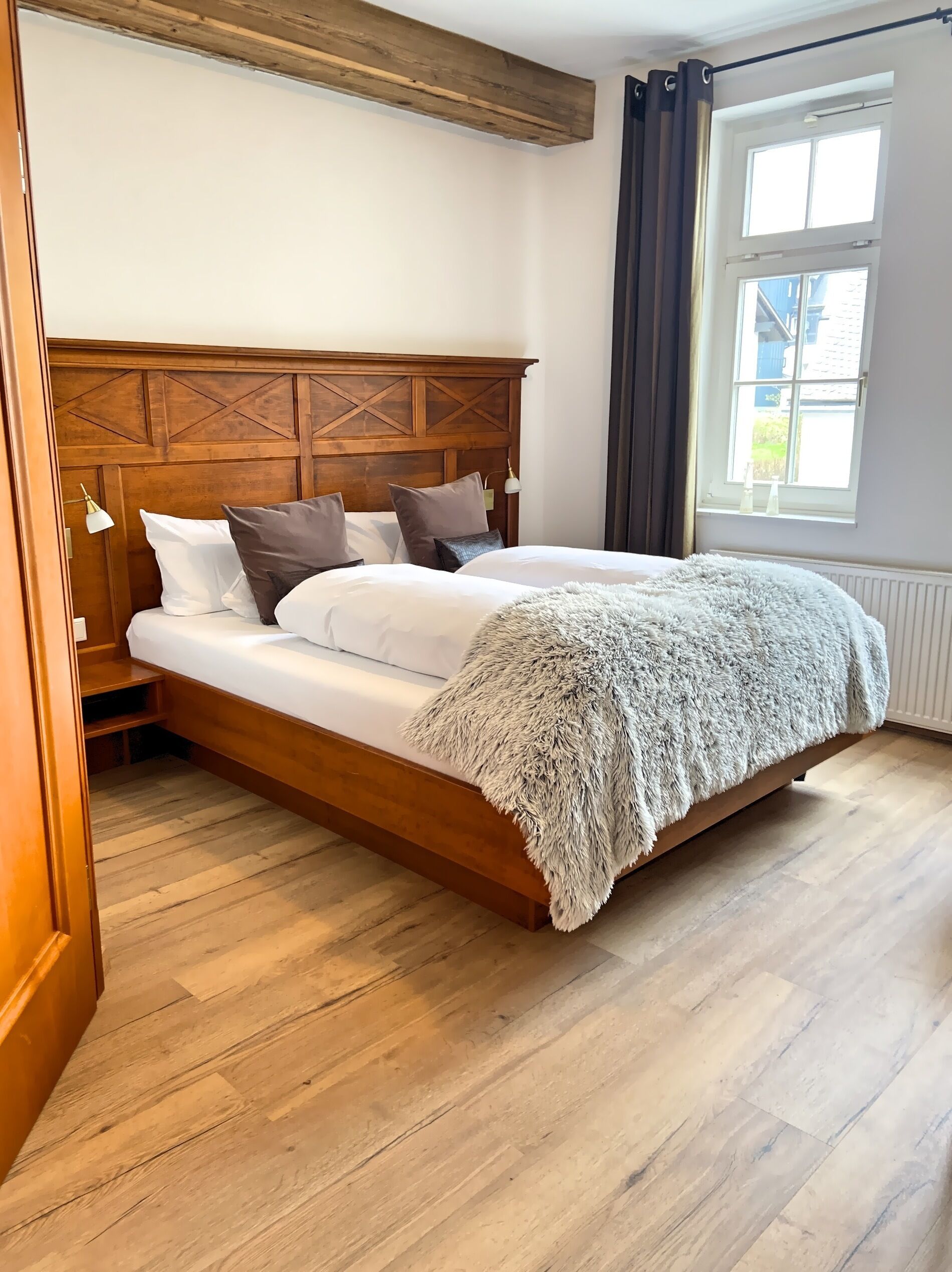 Una cama con cabecera de madera, ropa de cama blanca y un suave plaid.