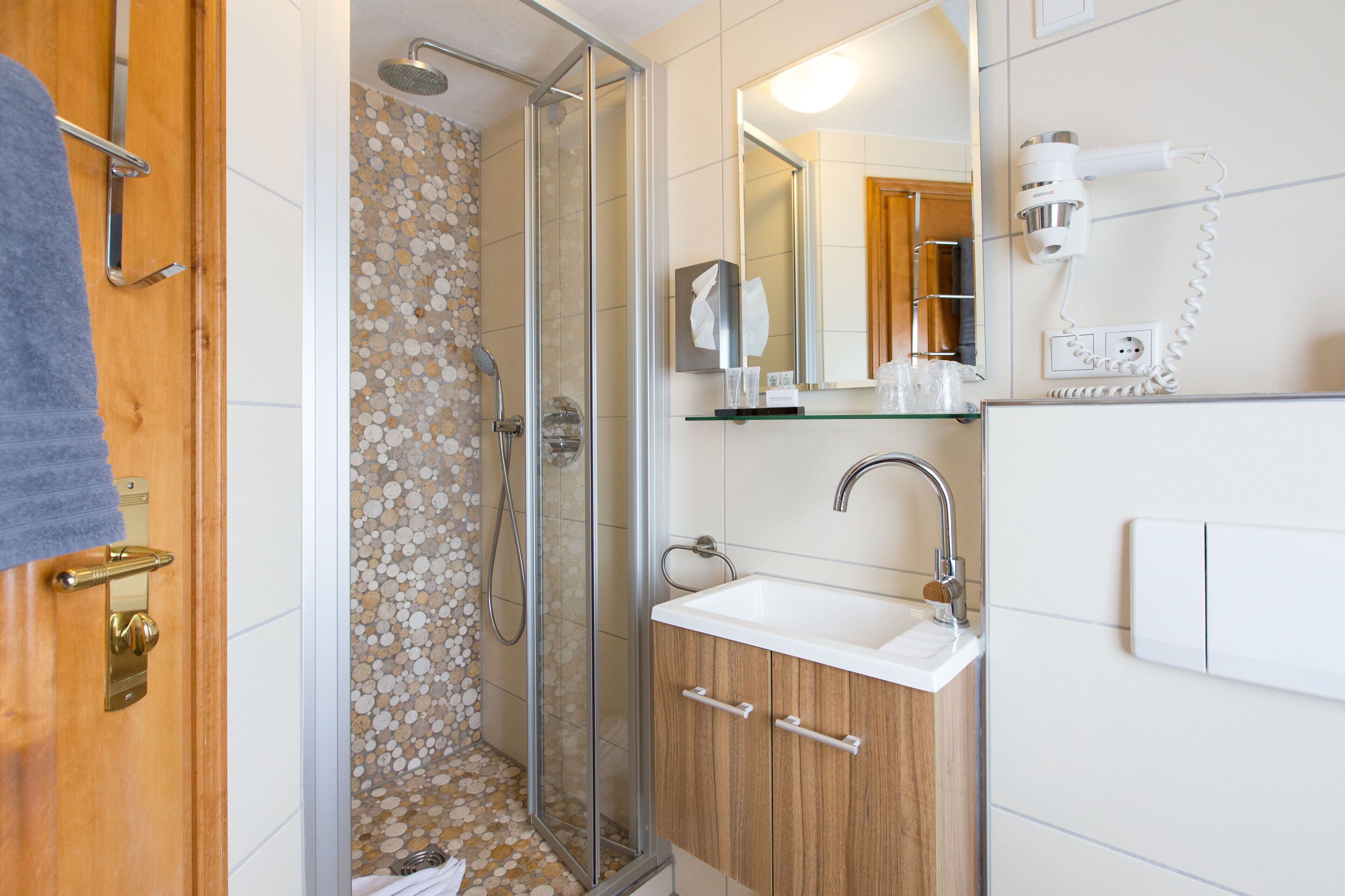Une salle de bain avec une douche à parois de verre, un lavabo blanc, des meubles en bois et un sèche-cheveux fixé au mur.