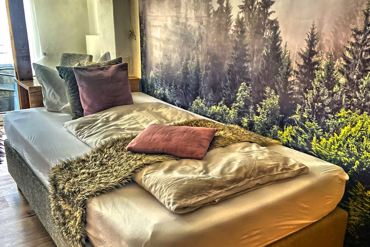 A bedroom with a bed, a mirror, and a forest mural on the wall.