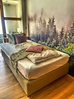 Un dormitorio con cama, espejo y un mural con motivos forestales en la pared.