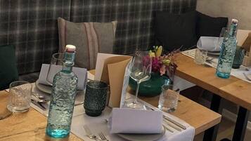 A dining area with wooden tables, clear glassware, and a plaid sofa in the background.