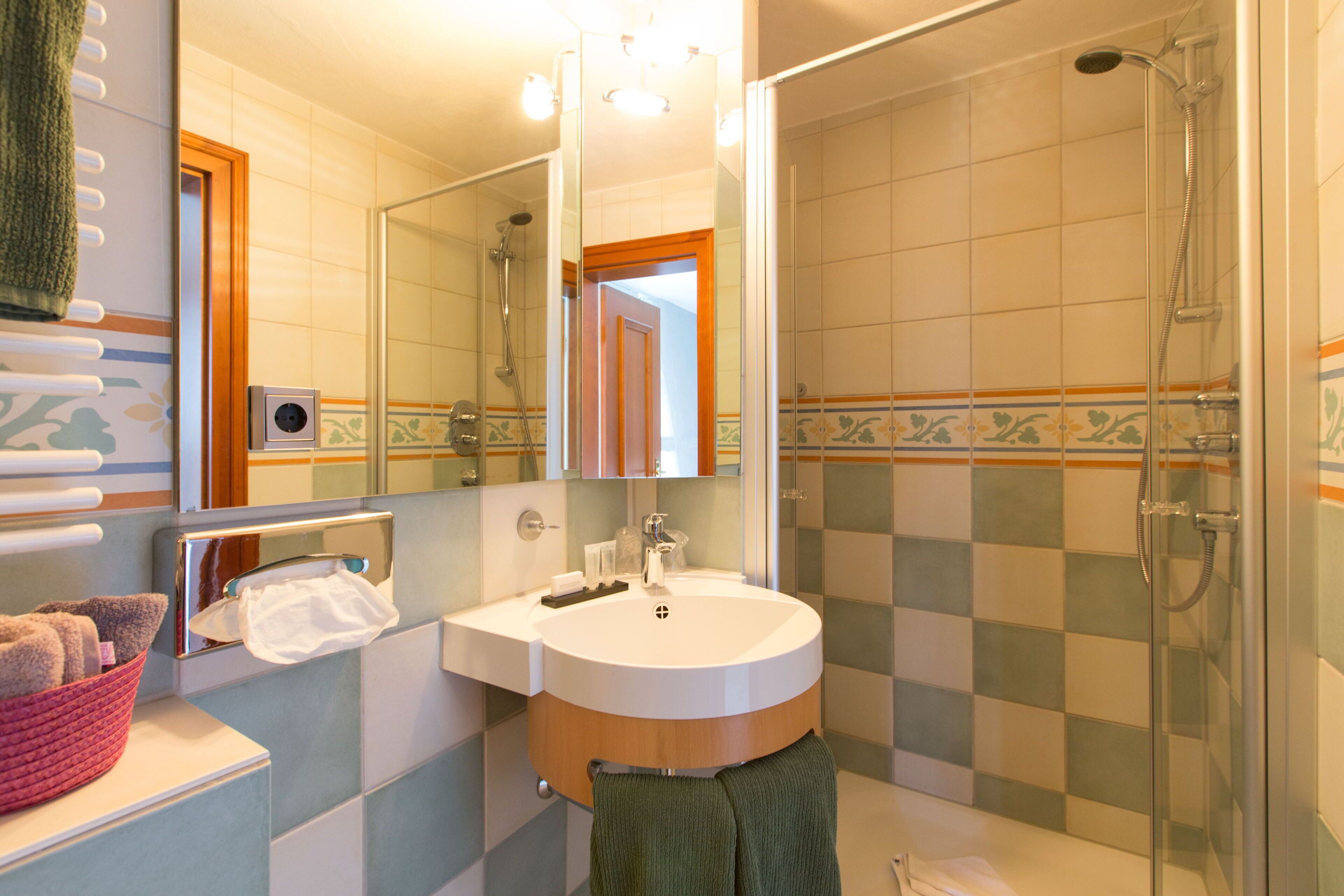A bathroom with a sink, mirror, shower, and towel rack.