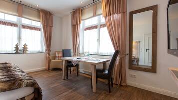 Ein Zimmer mit Holzboden, einem Esstisch mit Stühlen, einem großen Spiegel und Vorhängen.