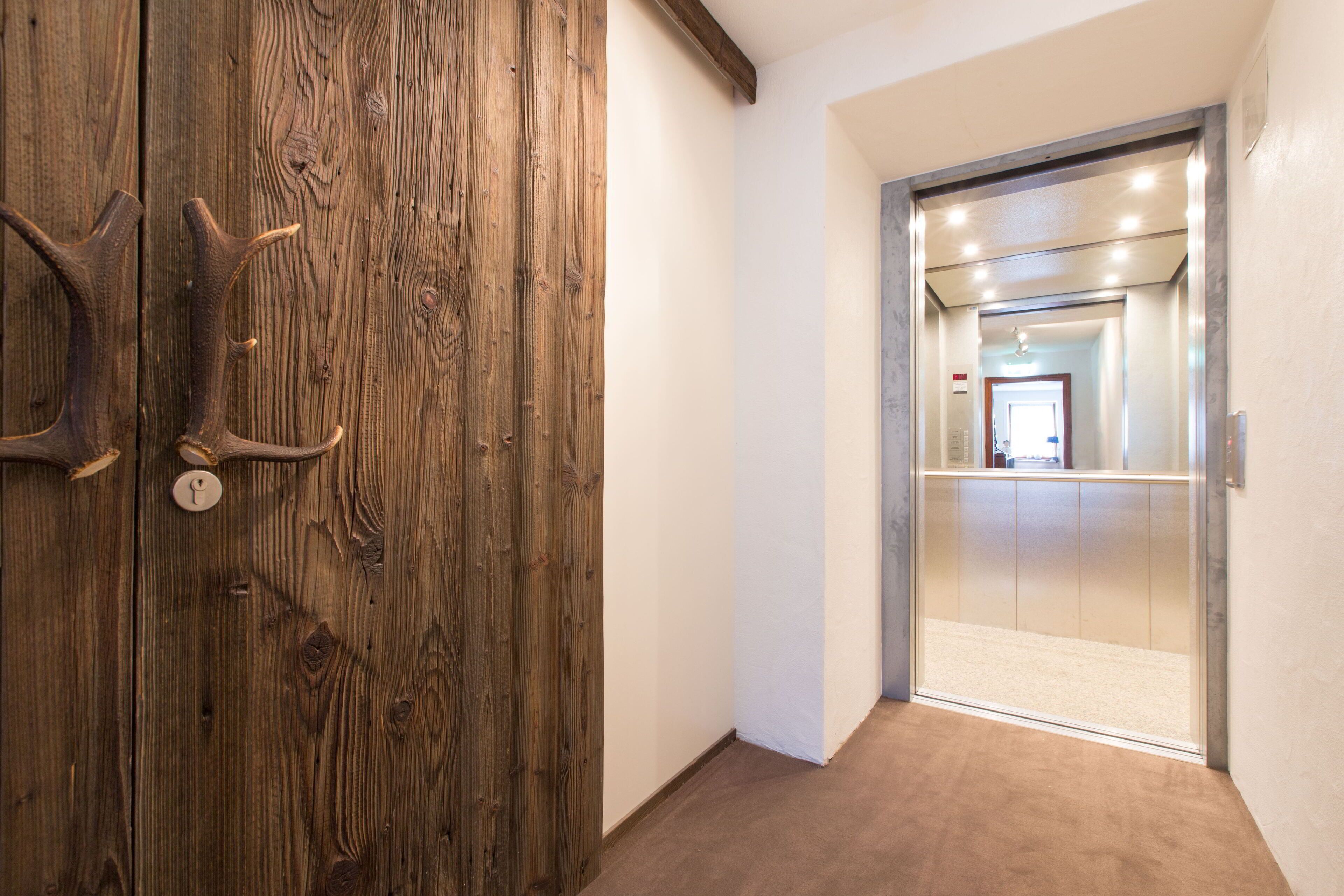Une porte en bois avec un trou de serrure, et un ascenseur moderne en arrière-plan.