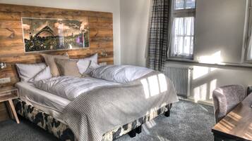 A bedroom with a bed, a nightstand, a chair, a window with curtains, and a wall-mounted artwork.