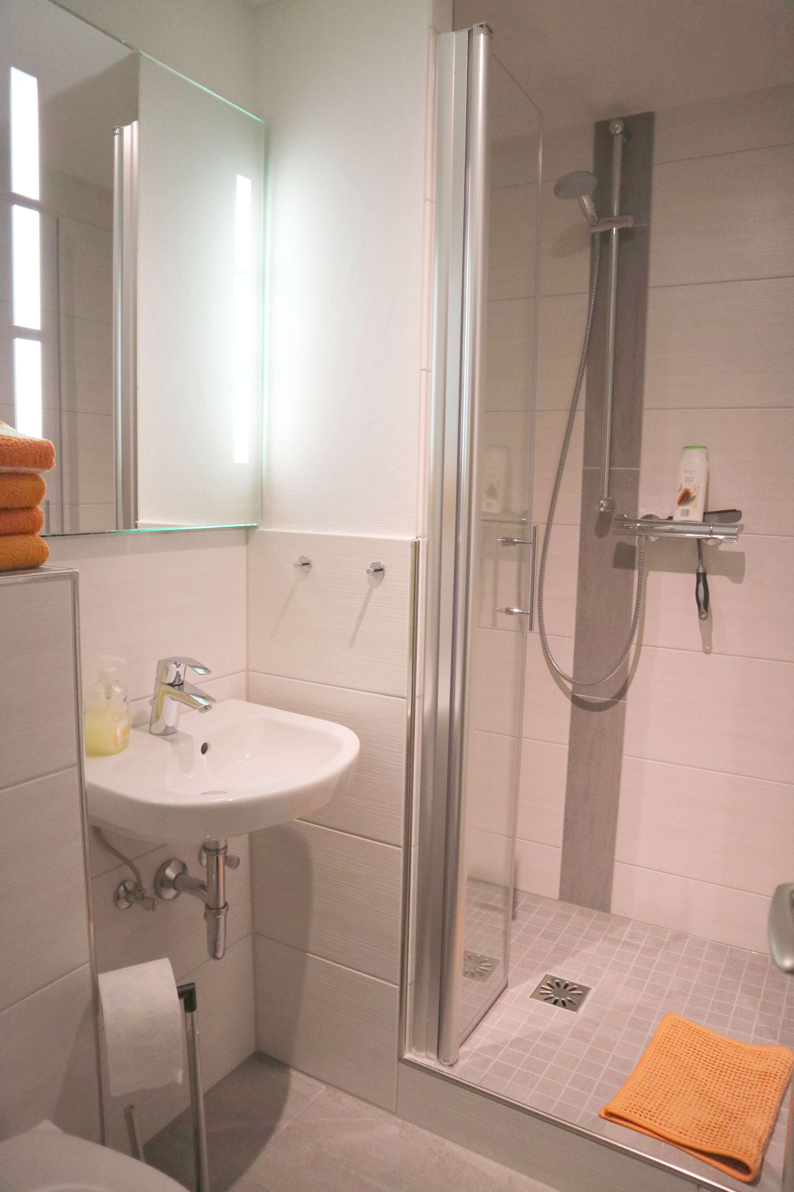 A modern bathroom with a glass-enclosed shower, a sink with a soap dispenser, and a towel rack.