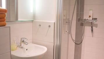 A modern bathroom with a glass-enclosed shower, a sink with a soap dispenser, and a towel rack.