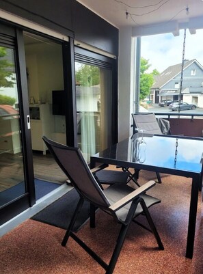 A modern dining area with a glass table and chairs, a sliding glass door leading to a kitchen, and a view of a residential street. - Hotel Nuhnetal (Winterberg)