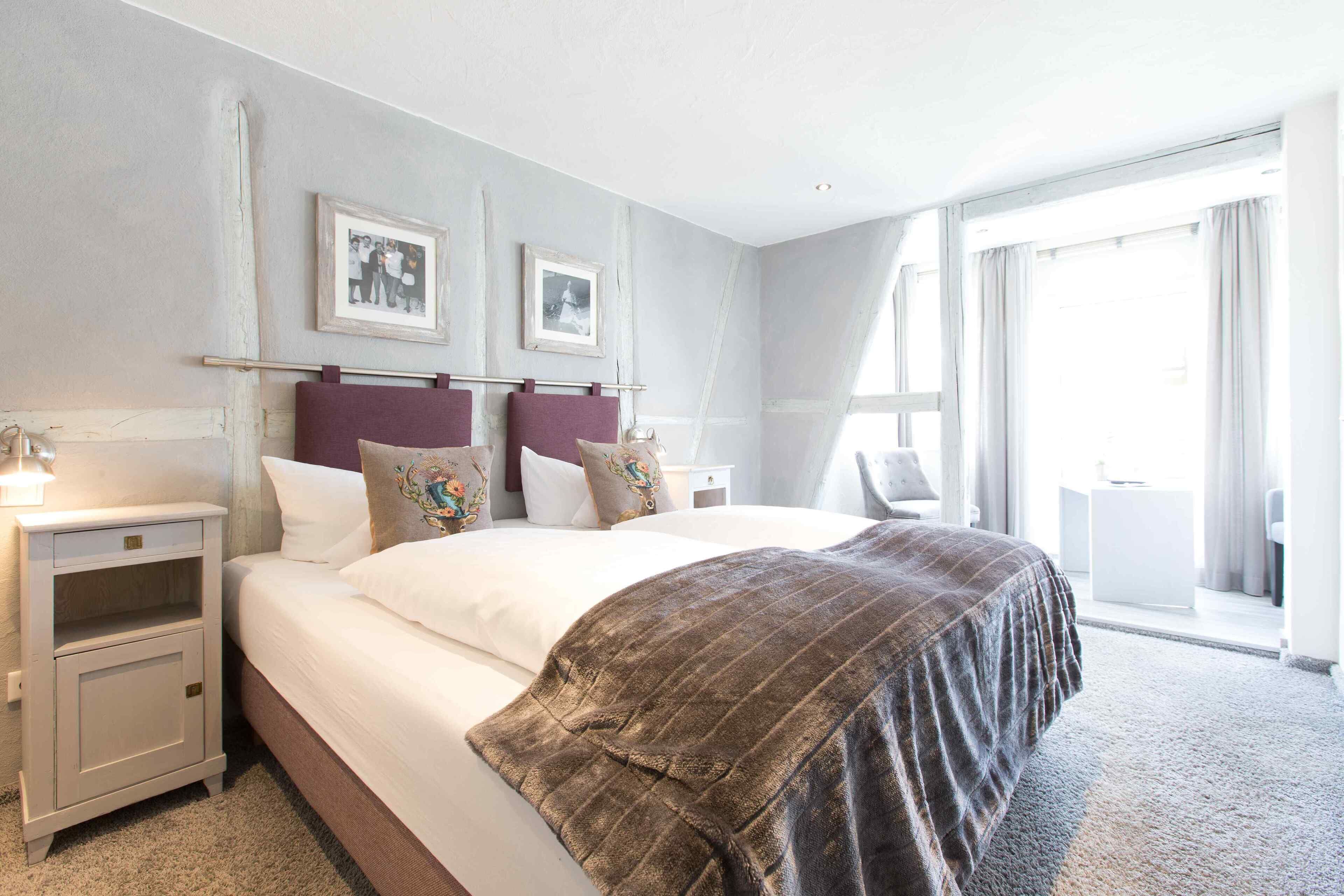A bedroom with a large bed, a nightstand, a dresser, and a window with curtains.